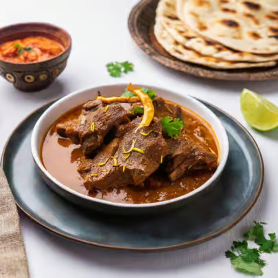 Kripa Indian Cuisine's rich lamb curry with naan bread, a side of sauce, and lime.
