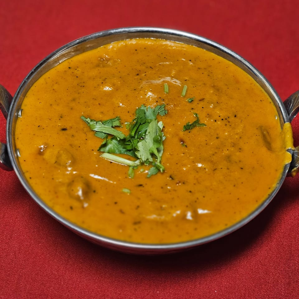 Kripa Indian Cuisine's creamy orange curry with cilantro in a metal bowl on a red tablecloth.