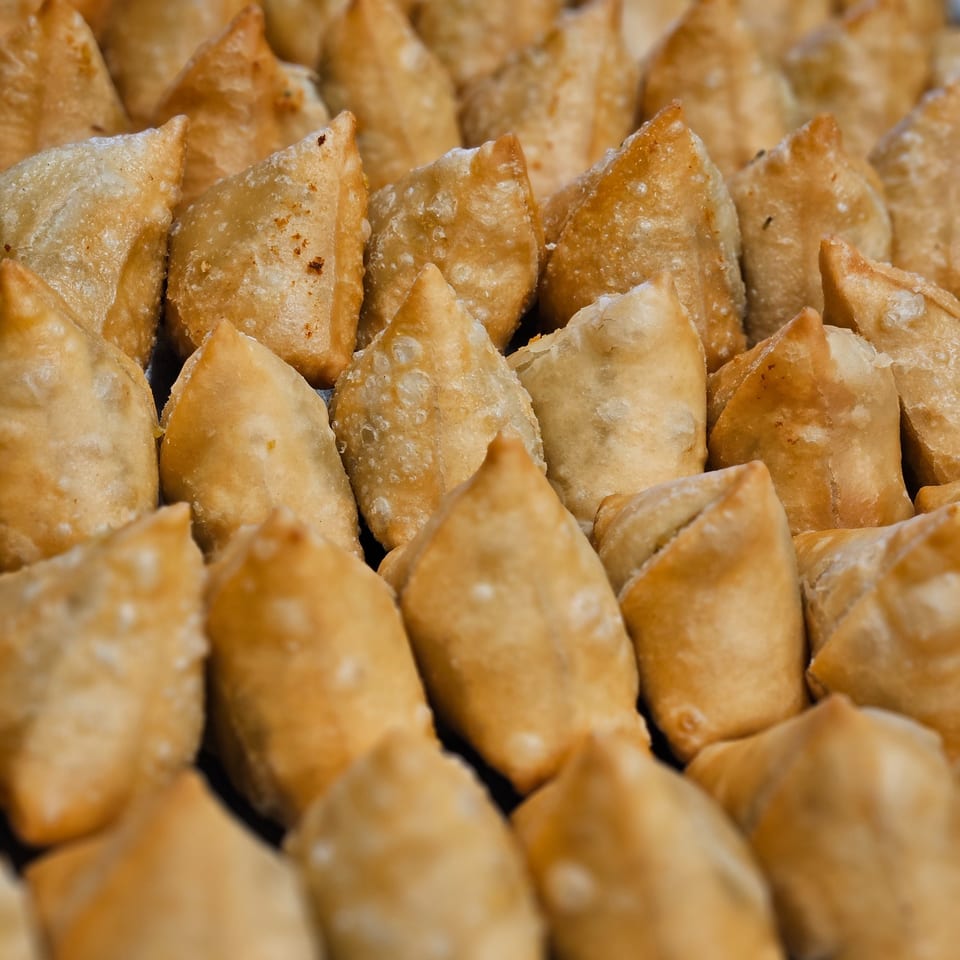 Close-up of many golden-brown, crispy samosas, a popular Indian appetizer, arranged in rows.