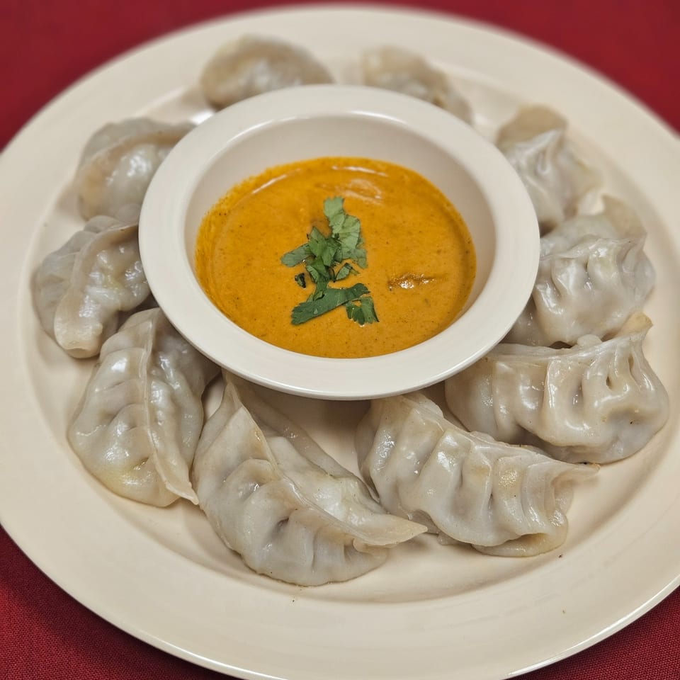 A plate of Kripa Indian Cuisine momos, steamed dumplings, arranged around a bowl of orange dipping sauce.