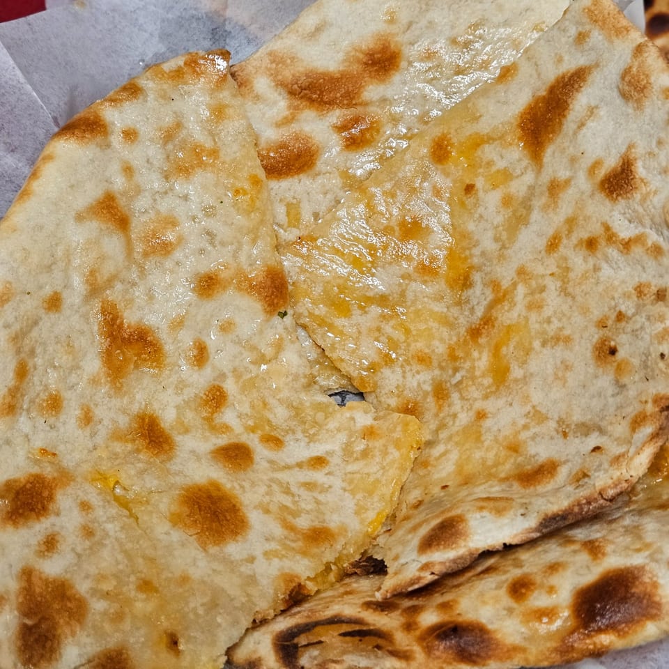 Close-up of golden-brown Indian naan bread, glistening with butter or oil, in a white paper-lined basket.