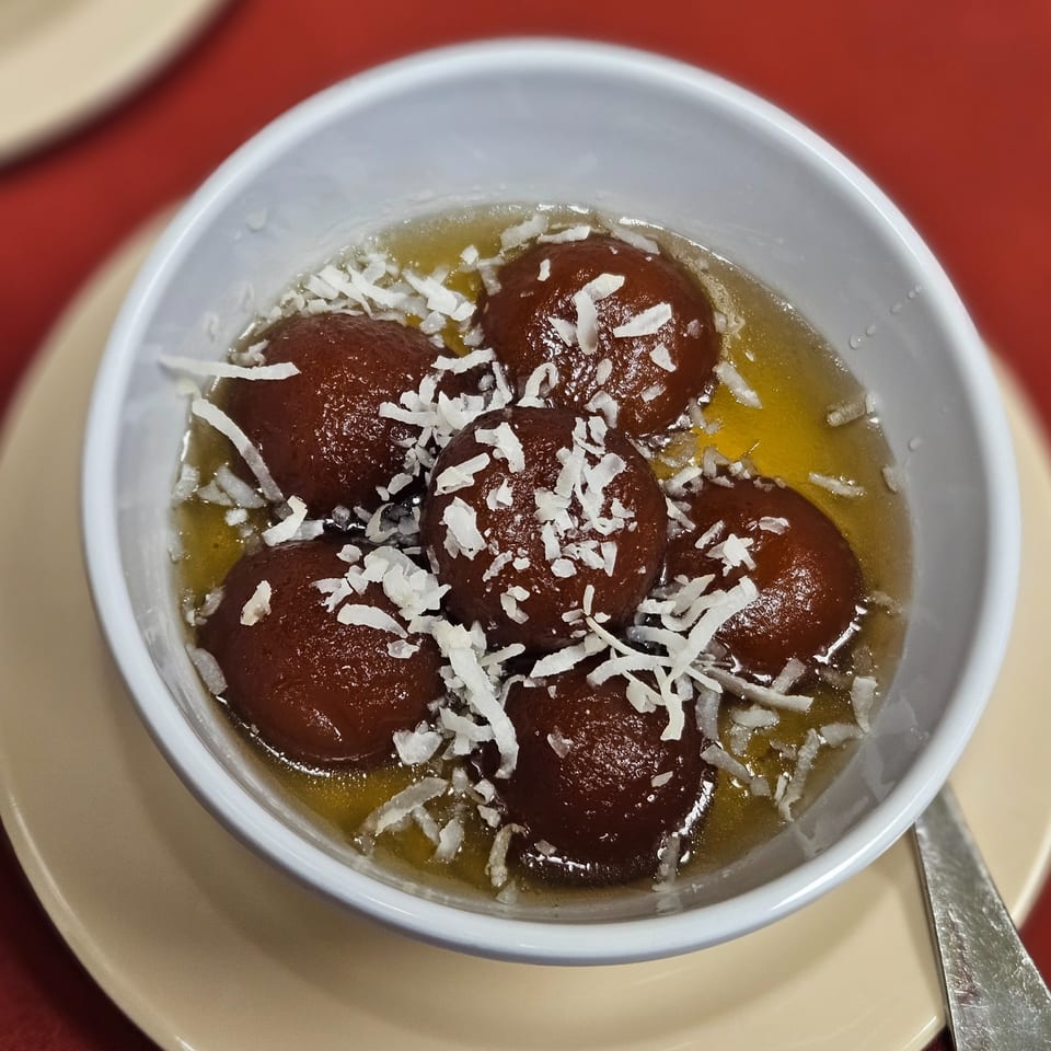 Gulab Jamun, an Indian dessert, in a white bowl with syrup and shredded coconut.