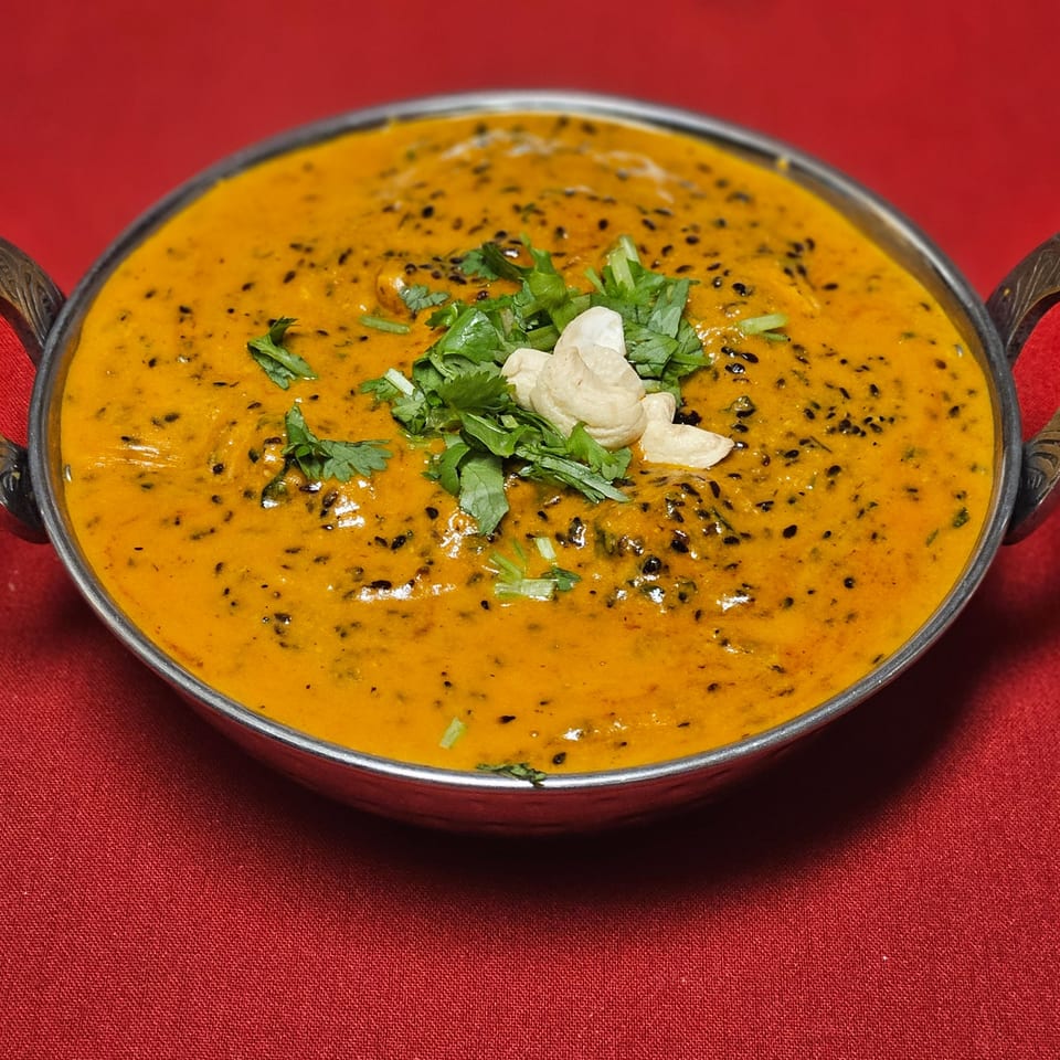 Kripa Indian Cuisine's creamy orange curry with black sesame seeds, cilantro, and cashews in a metal bowl.