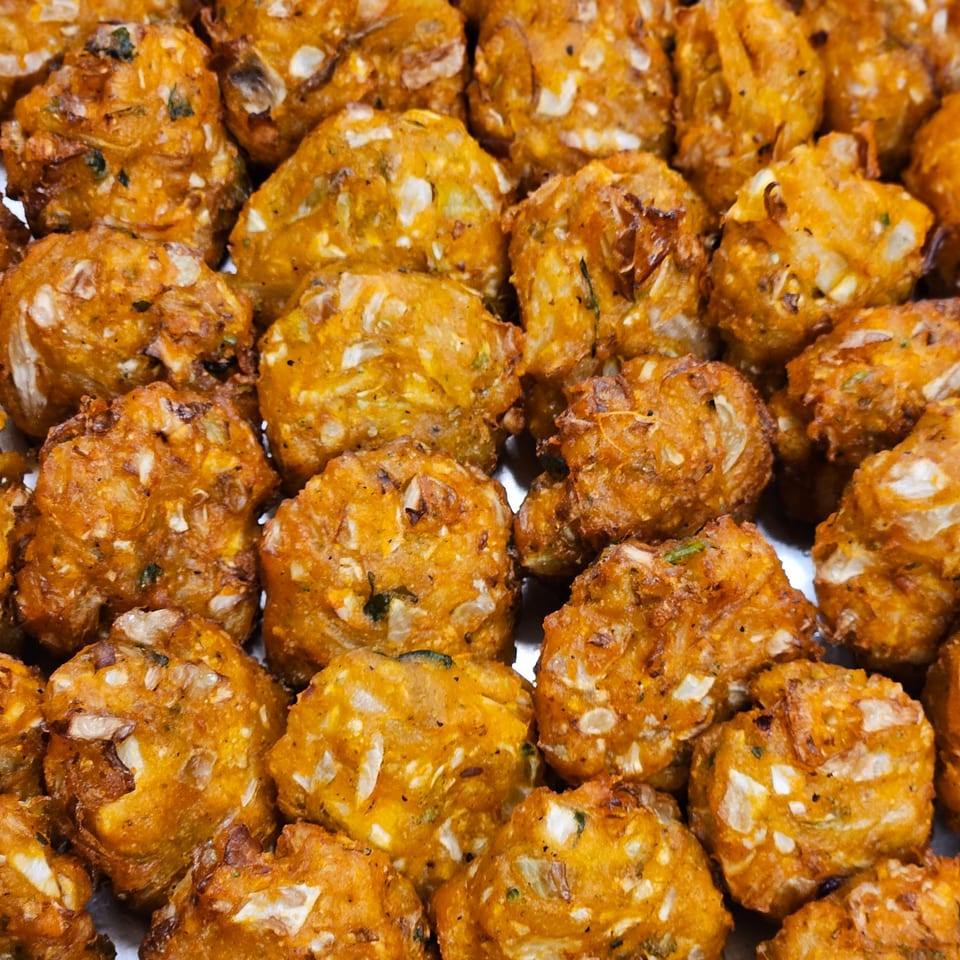 Close-up of numerous golden-brown Indian pakoras, showcasing their crispy texture and visible ingredients.