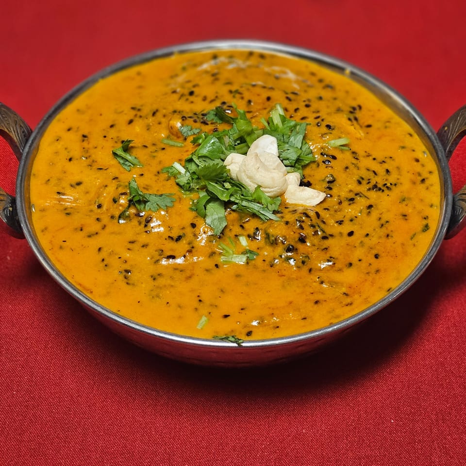 Kripa Indian Cuisine's creamy orange curry with black seeds, cilantro, and cashews in a metal bowl.