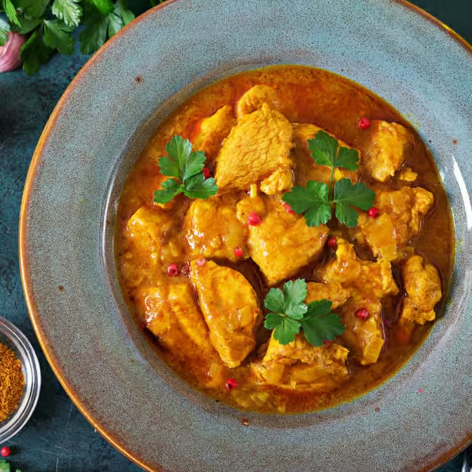 Close-up of Kripa Indian Cuisine's chicken curry, garnished with fresh parsley and red peppercorns.