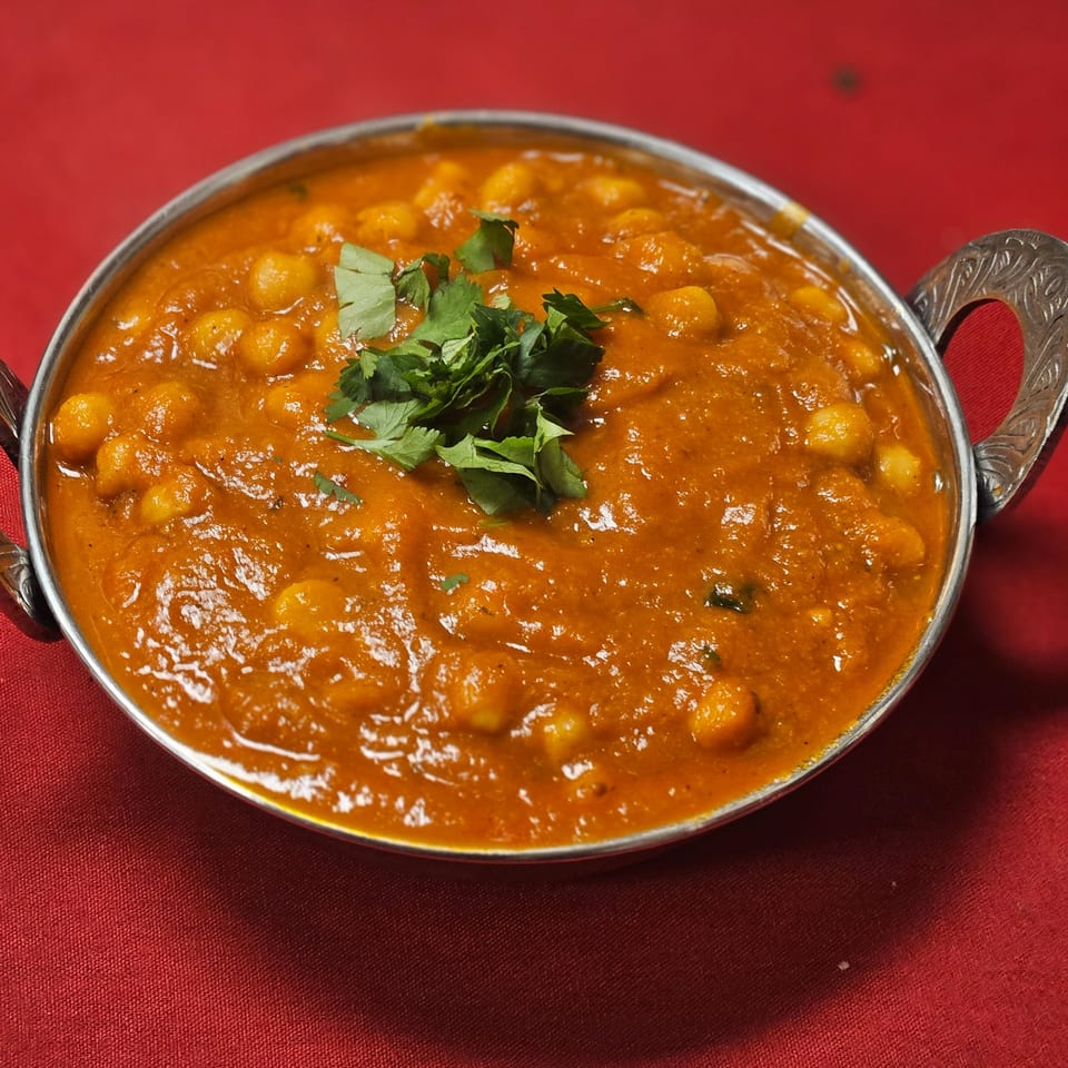Kripa Indian Cuisine's chana masala, a chickpea curry, garnished with fresh cilantro in a metal bowl.