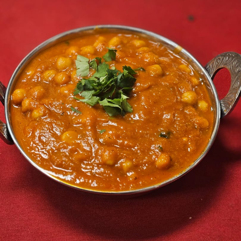 Kripa Indian Cuisine's chana masala, a chickpea curry, garnished with fresh cilantro in a metal bowl.