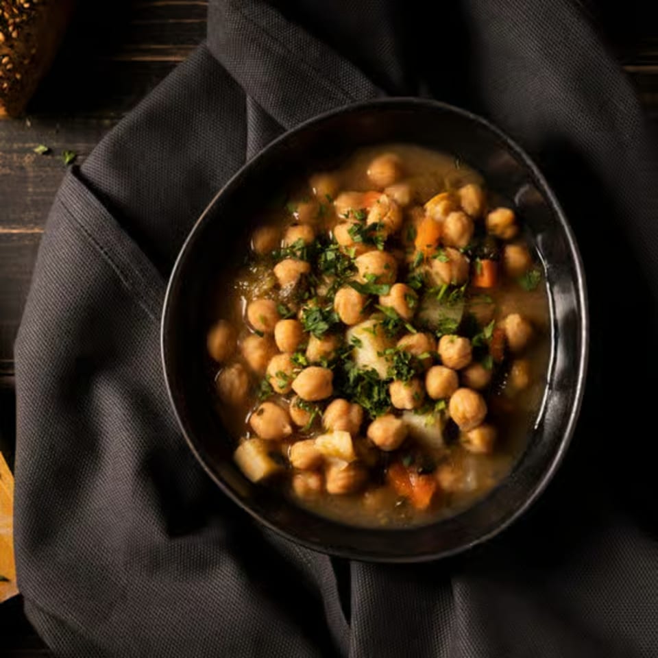 A black bowl of Kripa Indian Cuisine's chickpea stew with vegetables and herbs on a dark napkin.
