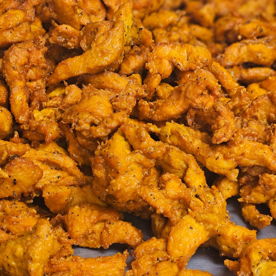 Close-up of golden-brown, bite-sized pieces of Indian chicken pakora, seasoned with black pepper.